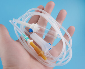 The infusion system lies on the palm of the hand on a blue background. Close-up. IV Set Infusion. Intravenous drip system.