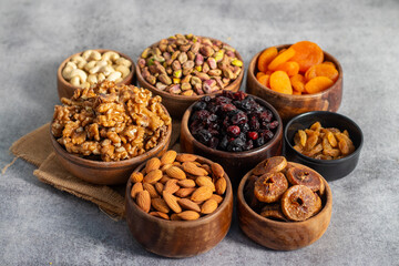 dry fruits and nuts—walnuts, almonds, cashews, pistachios, dried figs, apricots, raisins, and berries—beautifully arranged in wooden bowls on a gray surface.