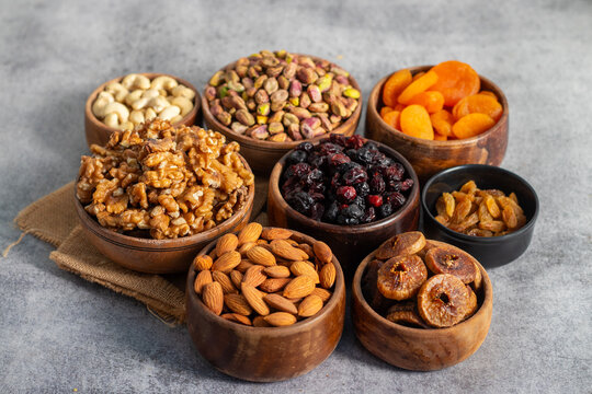 dry fruits and nuts&mdash;walnuts, almonds, cashews, pistachios, dried figs, apricots, raisins, and berries&mdash;beautifully arranged in wooden bowls on a gray surface.
