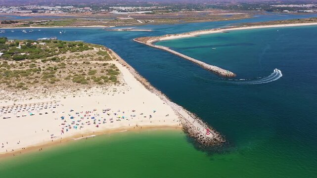 Aerial view drone shot of Tavira Portugal Algarve aerial shot of inlet with boat carving a wake near sandy point and sunfilled beach skipper and daytrippers enjoy coastal ride, shimmering