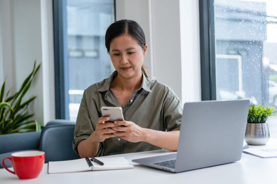 Businesswoman sitting at desk on couch in workplace or at home working on laptop and analyzing data on charts and graphs and writing on papers to make business plan and strategies for company
