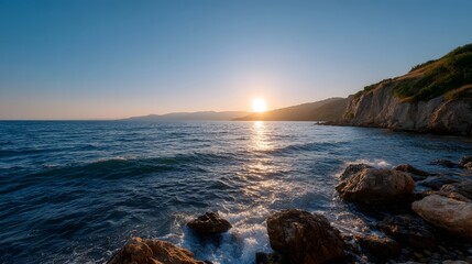 Golden hour illuminates a tranquil coastal landscape with calm sea rocky shore and distant mountains under a clear sky