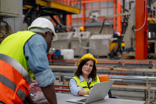 female engineer supervisor use computer laptop to discuss progress of production plan innovation with technician, team of diverse workers working together at industrial manufacturing factory
