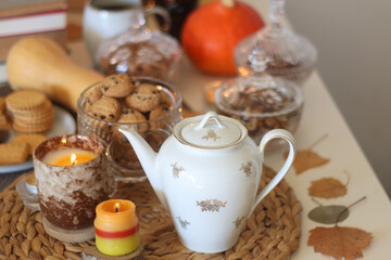 Lit candles, cookies, chocolate, nuts, tea, wine, pumpkins, books, reading glasses and autumn leaves on the table. Autumnal hygge at home. Selective focus.