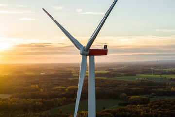 Close-up of modern wind turbines in a rural landscape at sunset. The blades rotate in warm evening light above green fields, symbolizing renewable energy and sustainability.