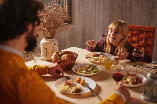 A joyful family dinner takes place in a cozy setting, featuring a smiling child enjoying a meal while seated with an adult. The table is adorned with plates of food and drinks.