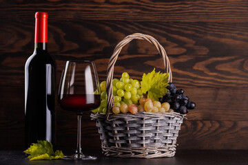 Naklejka premium Red wine bottle with a glass and basket of fresh grapes