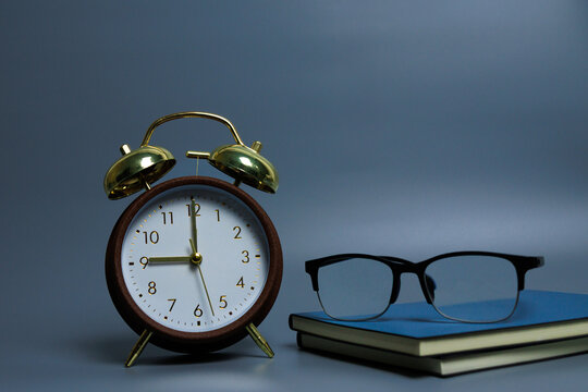 Classic alarm clock and eyeglasses on stacked notebooks with grey background, side view angle. Symbol of discipline, focus, planning, productivity, education, and modern lifestyle. - Powered by Adobe