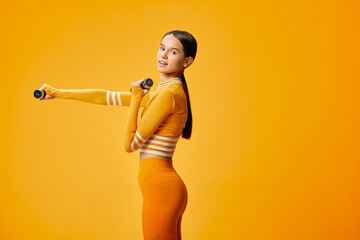 Fototapeta premium Woman in bright orange athletic wear holding dumbbells against a vibrant orange backdrop, showcasing fitness training, balance, and athletic confidence.