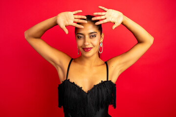 Confident latin woman smiling and raising hands over her head on a red background