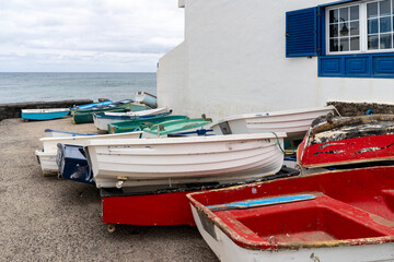 A collection of colorful rowboats sit on the shore near a white building with blue accents, by the calm ocean.