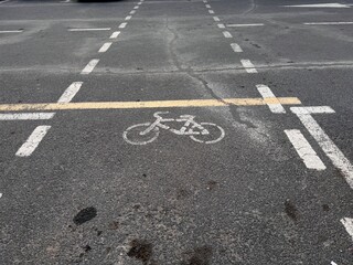 White bicycle symbol painted on dark asphalt, surrounded by road markings. Highlighting urban transport, ecology, and road safety. Cyclist, urbanism, travel.