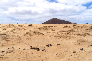 A scenic view of a volcanic mountain on La Graciosa, with sandy dunes and sparse vegetation under a...