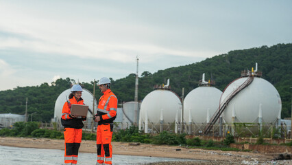 Petrochemical engineers in PPE conduct a site survey near LNG storage spheres. They use a laptop for data analysis and a radio for comms at the coastal refinery terminal.