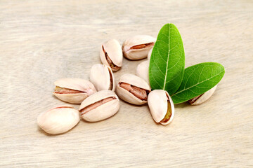 Pistachios and green leaves spilled on wooden background