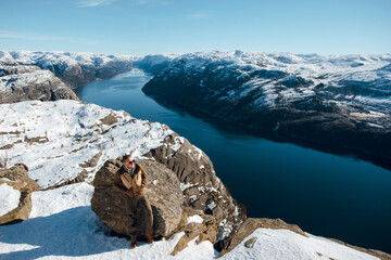 Man on Snowy Cliff Overlooking Fjord and Mountains