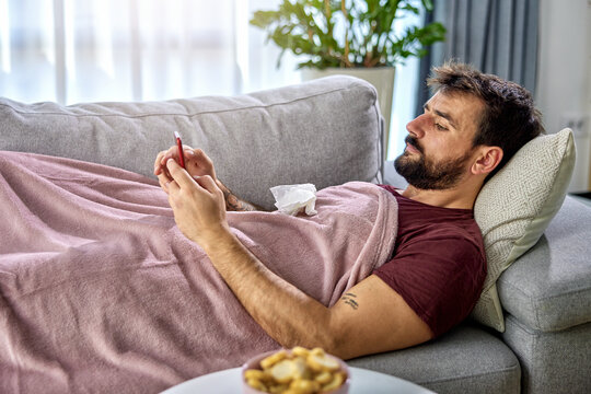 handsome bearded young man lying at home in isolation using a mobile phone