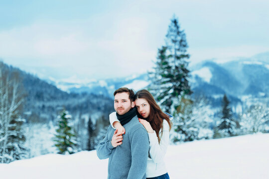 Young couple enjoys a snowy winter day in the mountains, embracing amidst the stunning landscape and pine trees while their cheeks are flushed from the cold