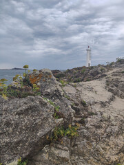 Coastal lighthouse standing on rocky shoreline under cloudy sky