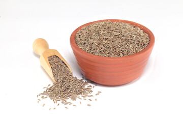  Cumin seeds spilled out of clay bowl and scoop on white background