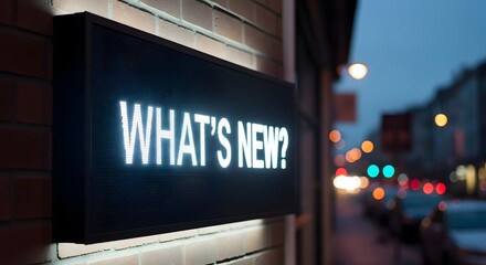Illuminated "WHAT'S NEW?" sign on a brick wall at dusk, with blurred street lights in the background.