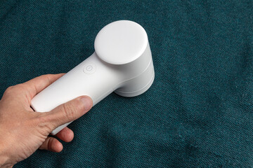 A compact white handheld lint remover is gripped by a person&rsquo;s hand