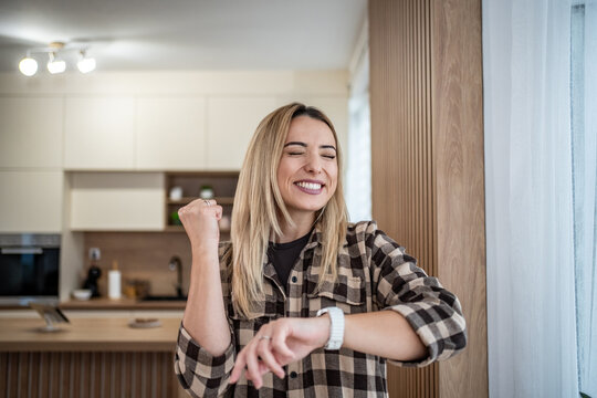 Happy woman celebrating success checking smartwatch at home - Powered by Adobe