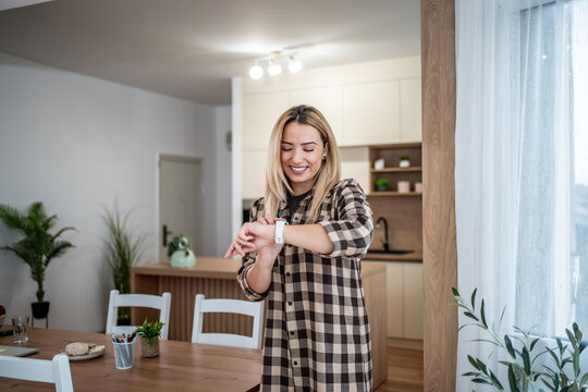 Woman smiling checking time on smartwatch at home