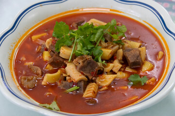 Spicy beef and tripe soup with noodles garnished with cilantro in red chili broth, hearty savory stew with aromatic herbs and comforting warmth