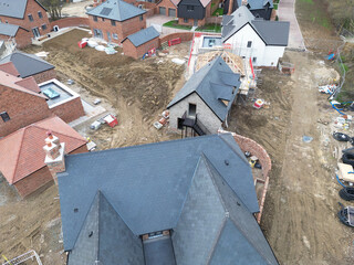 Low level drone inspection view of a new tiled roof and solar panel attached to a near completed family home on a British housing estate.  Smaller properties can be seen in the background.
