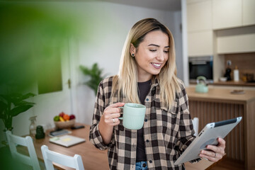 Woman smiling, drinking coffee and using tablet at home