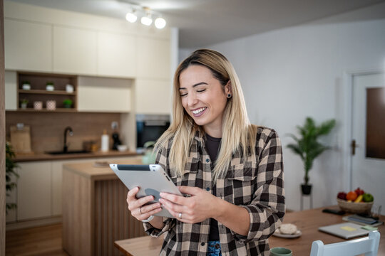 Young woman smiling while browsing on digital tablet at home