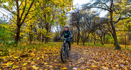 Beautiful middle-aged woman riding bicycle on path in forest in autumn. Front view