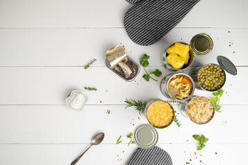 Various opened canned foods, lids, and a spoon on a white table with herbs and spices scattered around.
