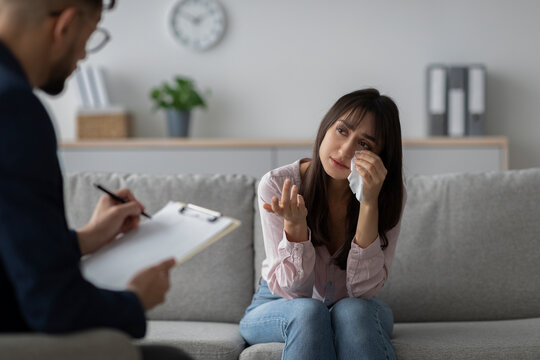 In a calming therapist's office, an Arab woman is sharing her feelings while crying during a counseling session. A male therapist is listening intently and taking notes. - Powered by Adobe