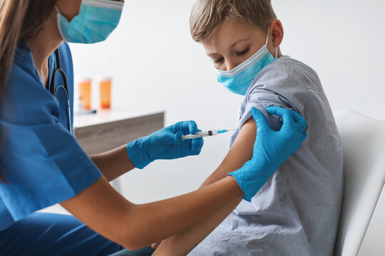 A nurse is giving a Covid-19 vaccine to a young boy in a clinic. The child is wearing a face mask, showing readiness for vaccination to ensure protection against the virus.