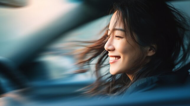 A woman is driving a car while her hair is flowing in the wind, creating a sense of freedom and adventure. The scene captures her joyful expression during this enjoyable drive.
