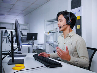 Concentrated Asian Businessman working in call center office. Male Customer Service Agent working on computer wearing headset with telemarketing, Help desk and Online Consulting to help client.