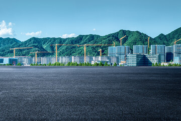 Empty asphalt road with a new real estate construction site and green mountain landscape in the background on a sunny day.