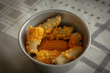 Boiled corn cobs in a metal bowl on a patterned tablecloth. A simple, rustic, and healthy snack.