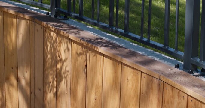Close-up of a modern fence featuring vertical wood cladding and metal railing under sunlight. Contemporary small architecture and outdoor design concept.