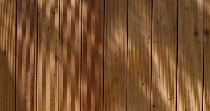 Natural wooden facade with sunlight and tree shadows creating a warm organic texture. Perfect background for architecture, design, or nature concepts.