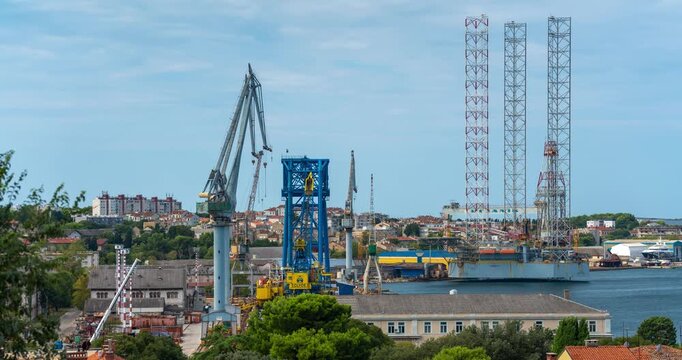 Pula, Croatia - August 18, 2025: Timelapse. Large coastal shipyard with cranes, metal structures, and docked platforms surrounded by buildings and calm blue water