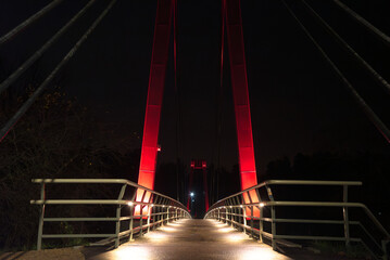 Symmetrical night view of illuminated pedestrian bridge with glowing red supports and handrails, creating a dramatic perspective.