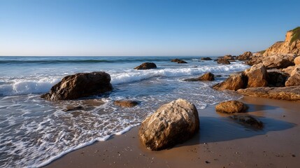 A serene beach scene with golden hour light illuminating waves crashing against rocky shores under a clear blue sky