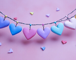 Pastel heart garland hanging against a pink background with scattered heart confetti decorations