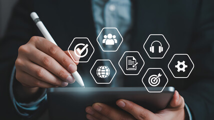 Modern professional uses stylus on tablet interacting with digital business icons for strategy, teamwork, global reach, and task management