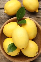 Fresh lemons with green leaves and bowl on wooden table, flat lay