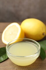 Lemon juice in bowl, leaves and fresh lemons on wooden table, closeup