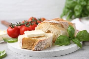 Slices of baguette with butter, basil and tomatoes on light grey table, closeup